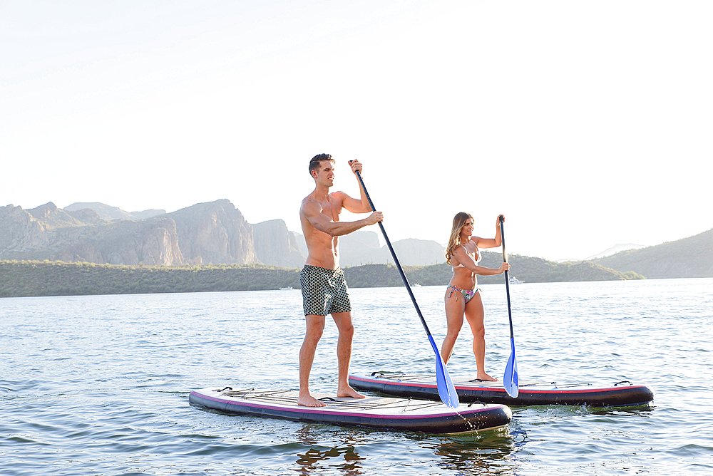 Couple standing on paddleboards in river