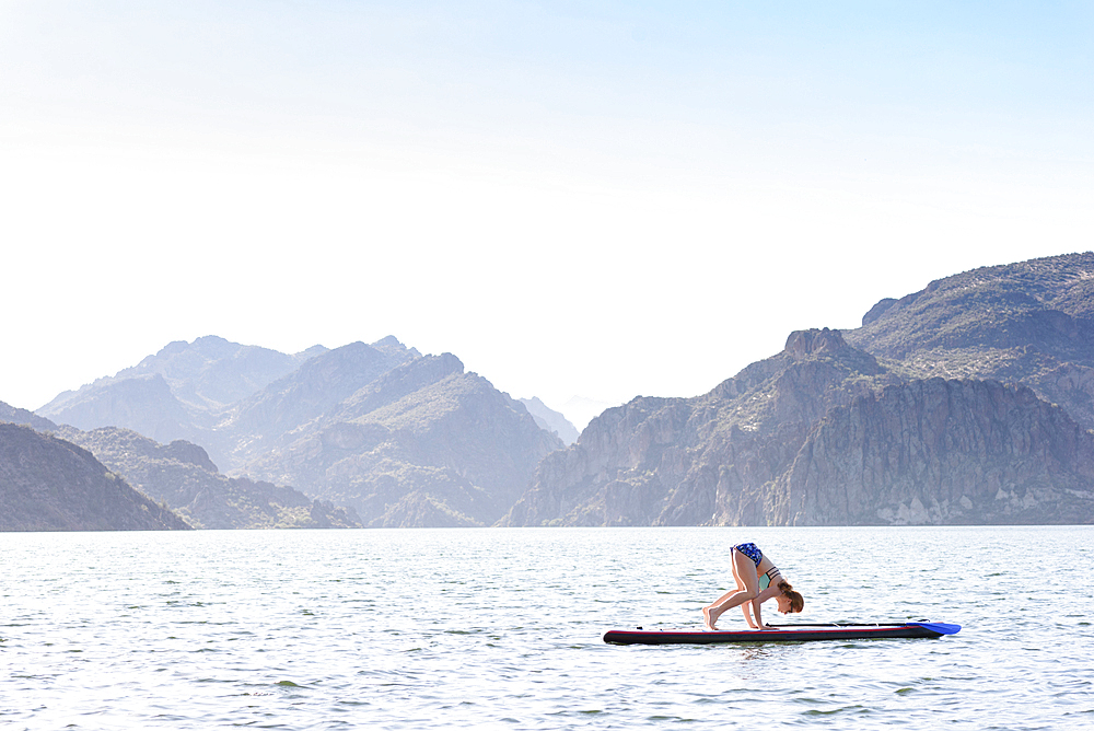 Caucasian woman stretching on paddleboard in river