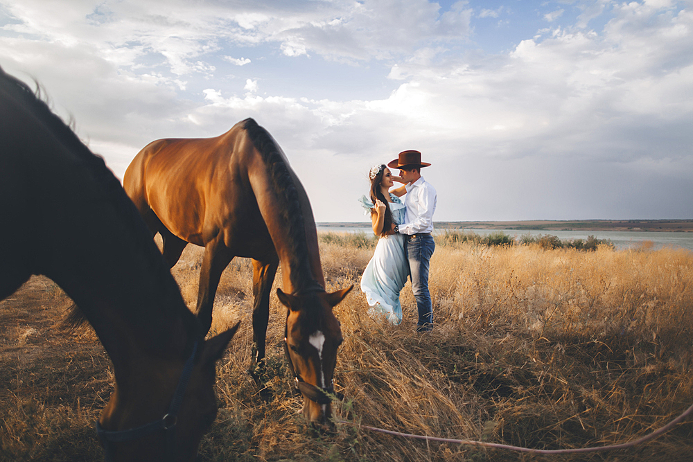 Horses grazing near Caucasian woman hugging cowboy