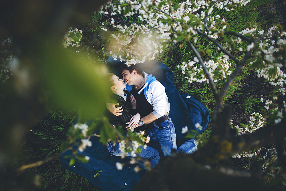 Caucasian couple laying in grass under flowering trees