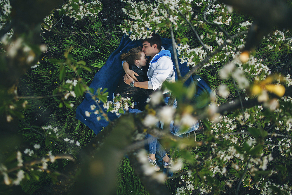 Caucasian couple laying in grass under flowering trees