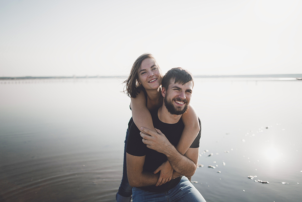 Caucasian man carrying woman piggyback on beach