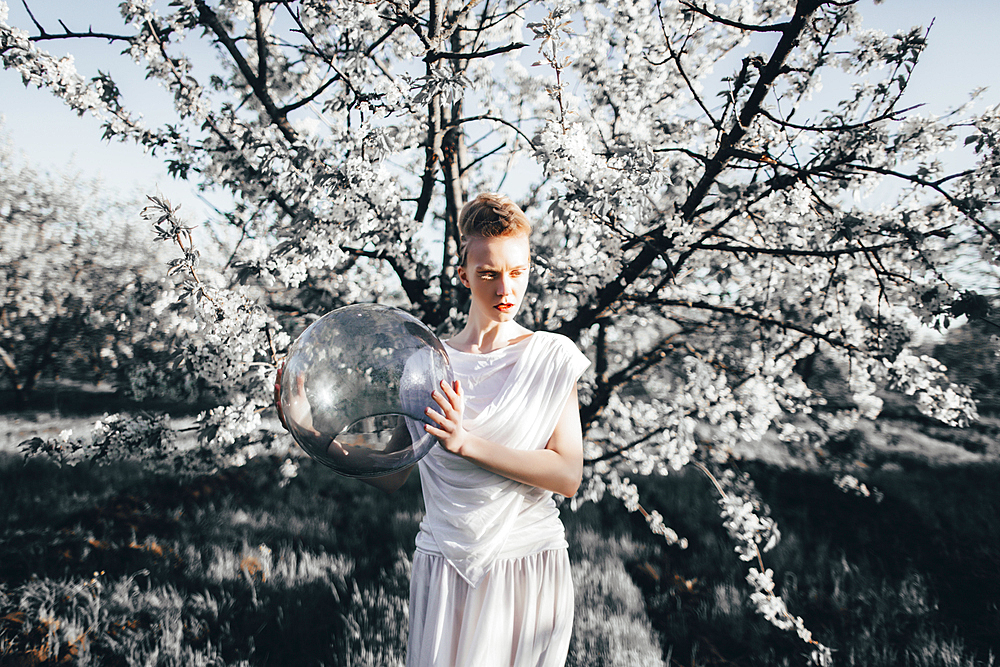 Unusual Caucasian teenage girl holding glass helmet near tree