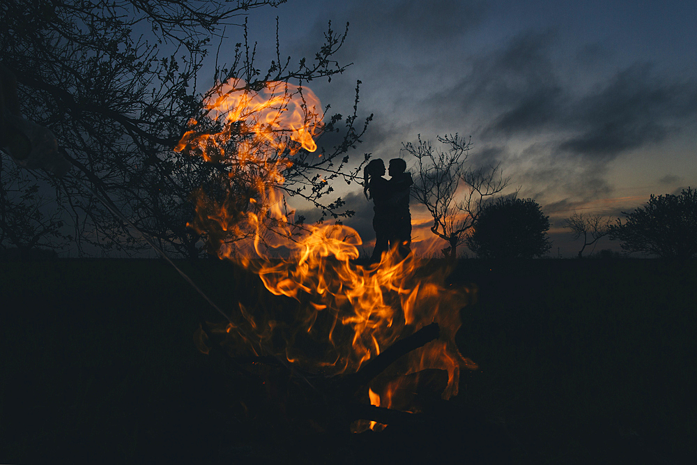 Silhouette of Caucasian couple kissing near fire