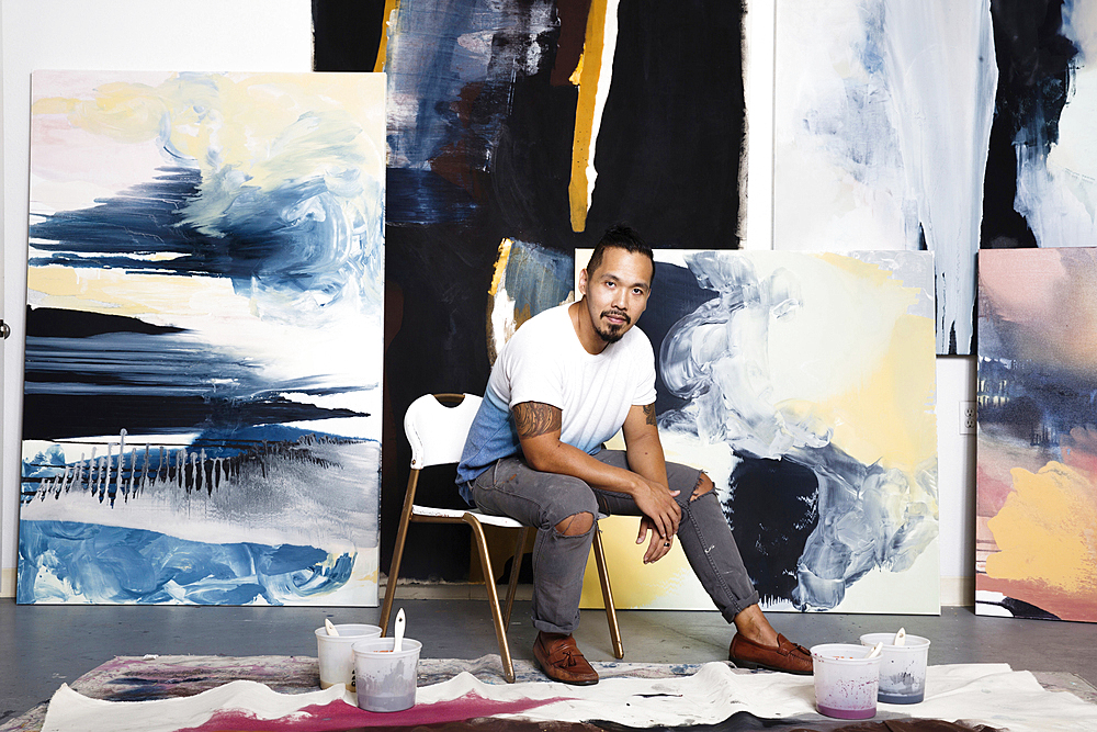 Pacific Islander artist sitting with paintings