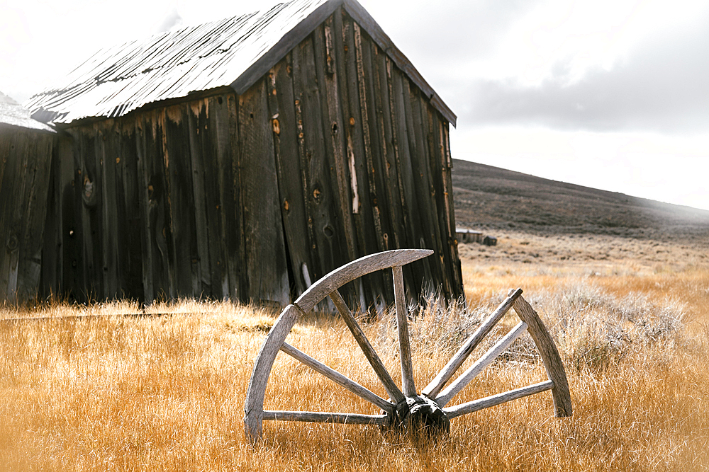 Broken wooden wheel in grass near rustic building