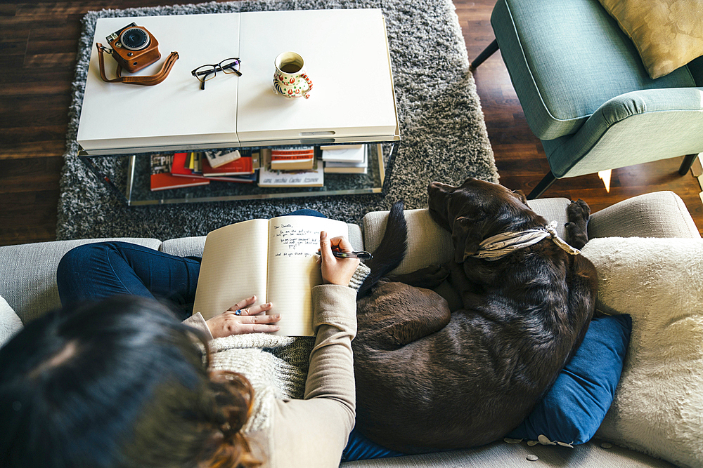 Mixed Race woman on sofa with dog writing in journal