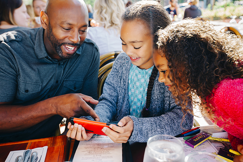 Father ad daughters texting on cell phone at restaurant