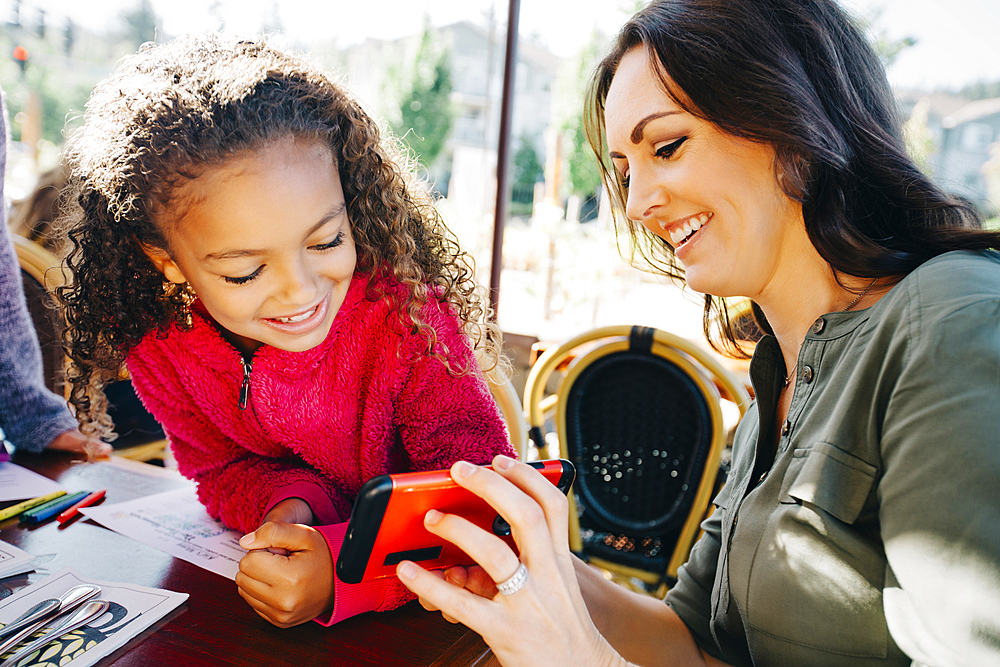 Mother and daughter texting on cell phone in restaurant