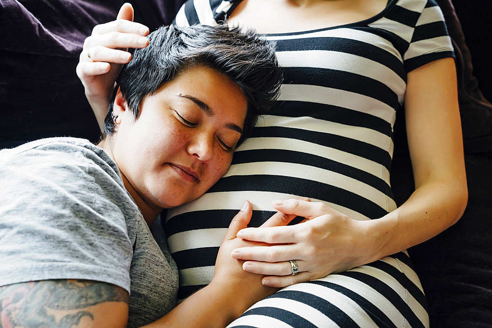 Pregnant lesbian couple cuddling on sofa