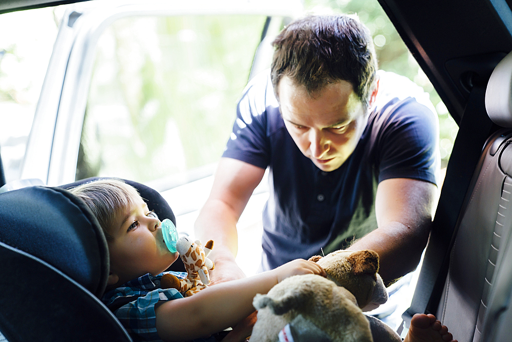 Father buckling son into car seat