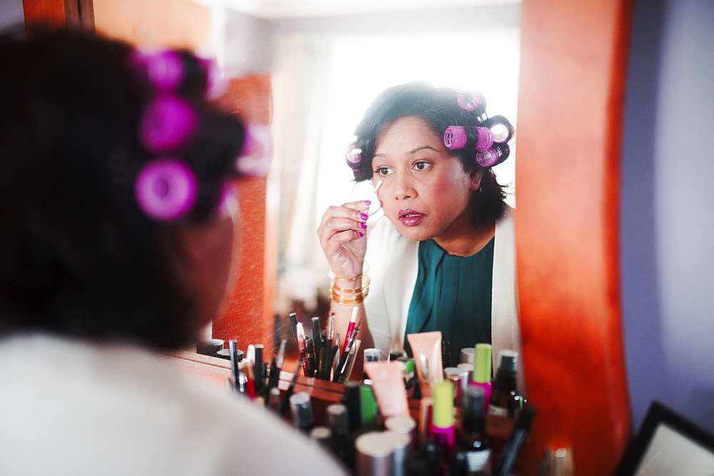 Indian woman wearing curlers applying makeup