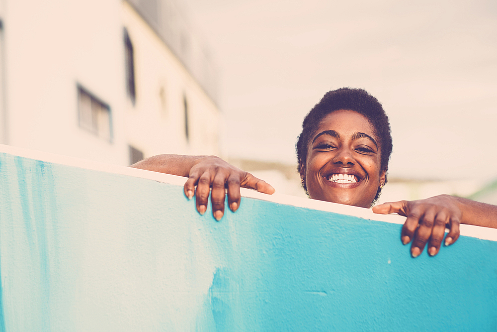 Smiling African American woman peering over blue wall