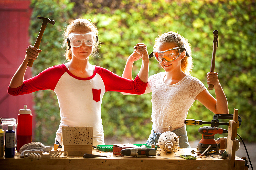 Sisters flexing muscles and holding hammers