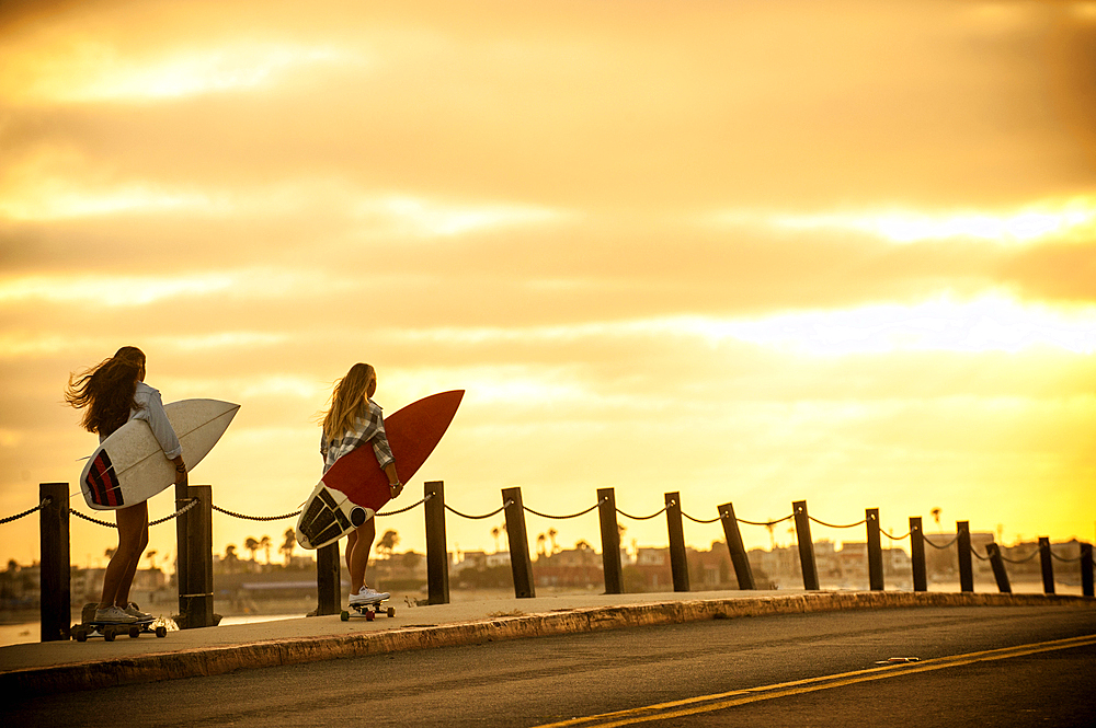 Teenage girls carrying surfboards on skateboards