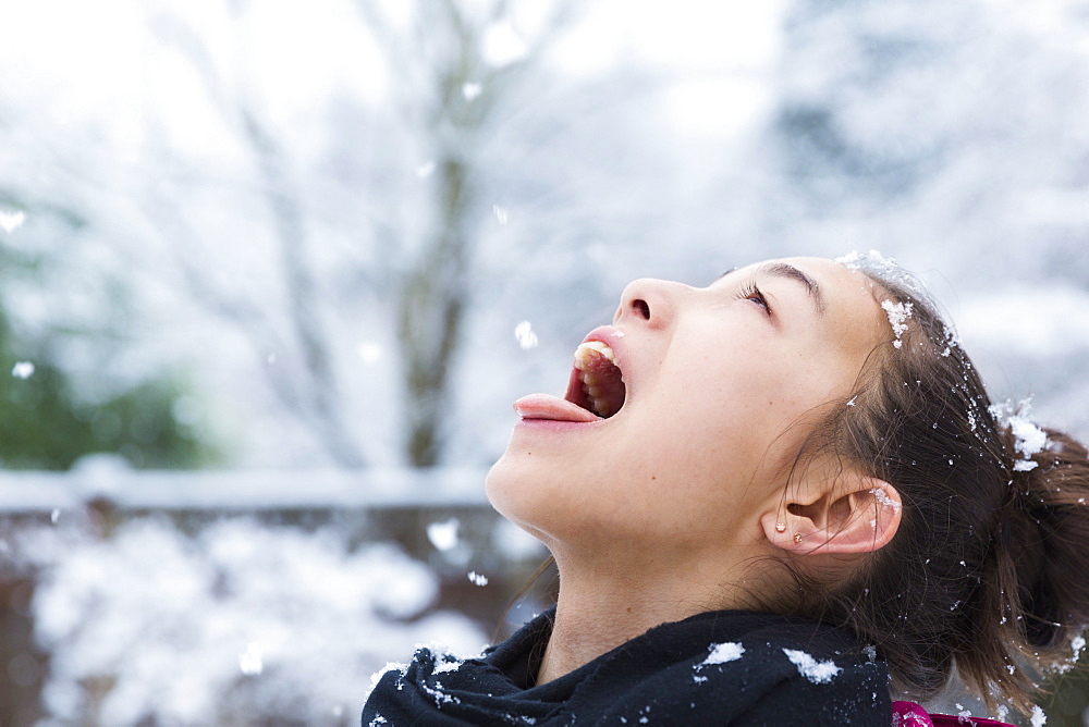 Mixed Race girl catching snowflakes on tongue