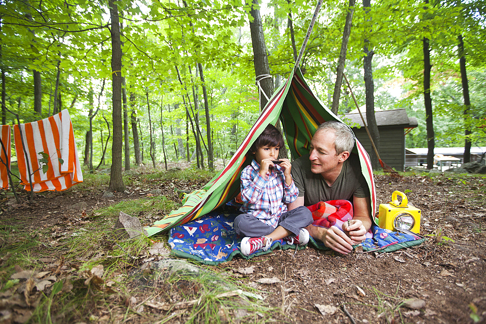 Father watching son playing harmonica in blanket fort