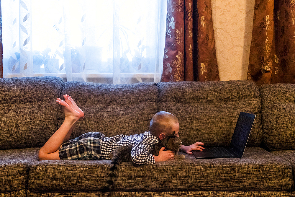 Caucasian boy laying on sofa with cat using laptop