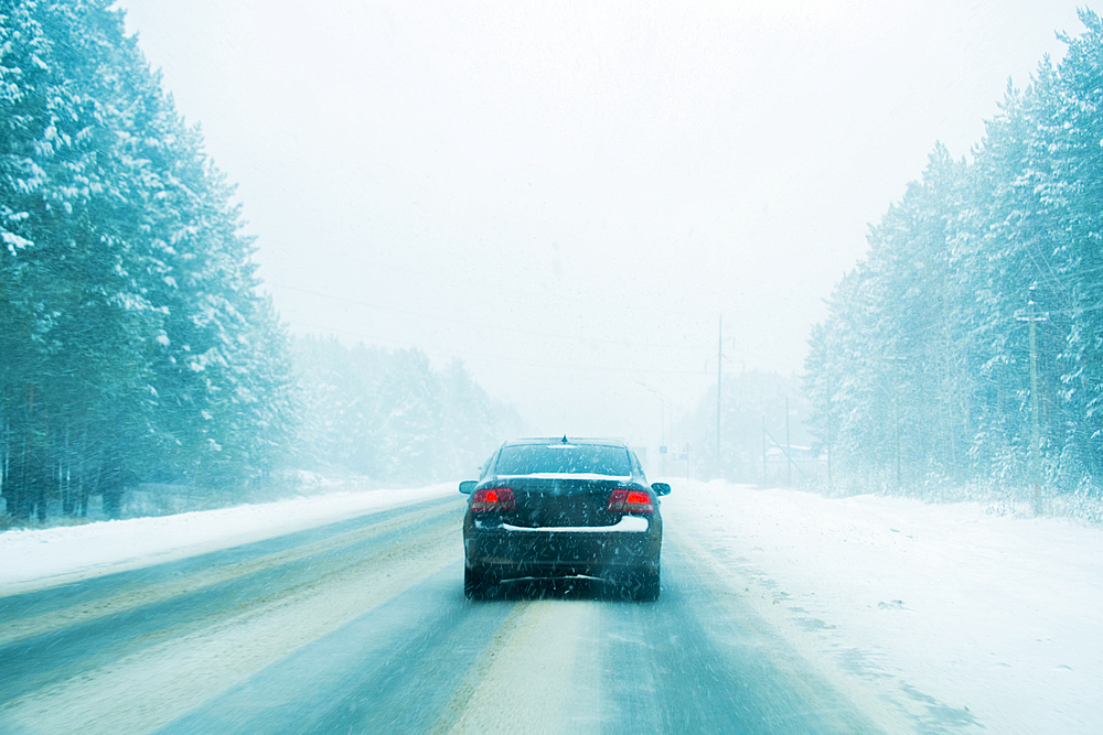 Car driving on tree-lined road in winter