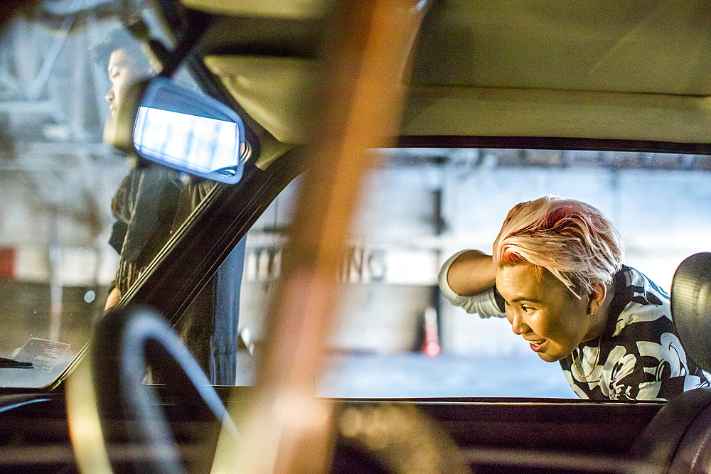 Androgynous Asian woman checking hair in side-view mirror