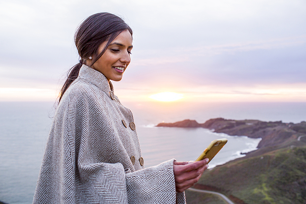 Smiling Indian woman texting on cell phone near shore