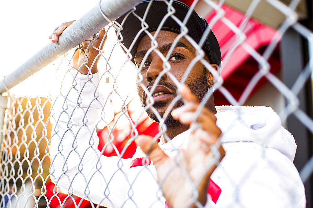 Curious Black man leaning on chain-link fence