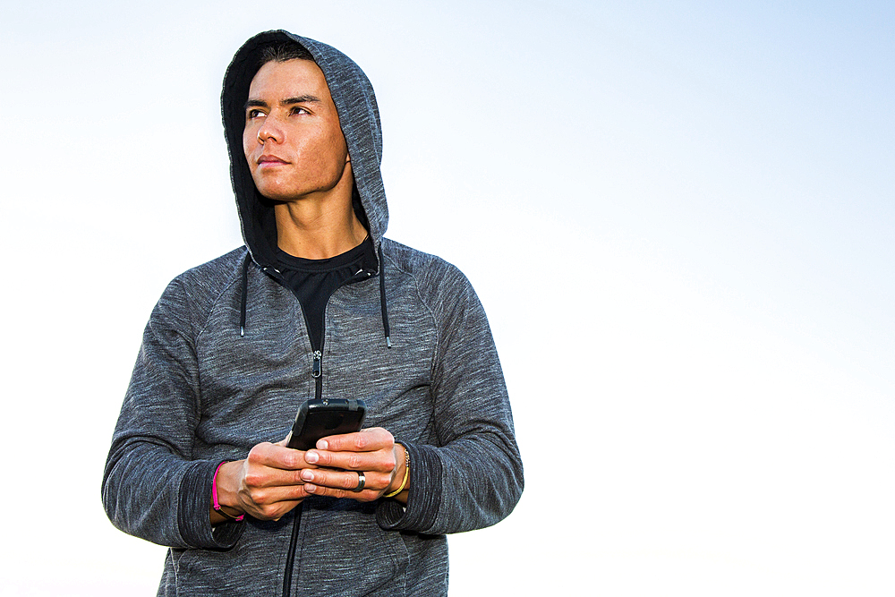 Mixed Race man wearing hoody texting on cell phone