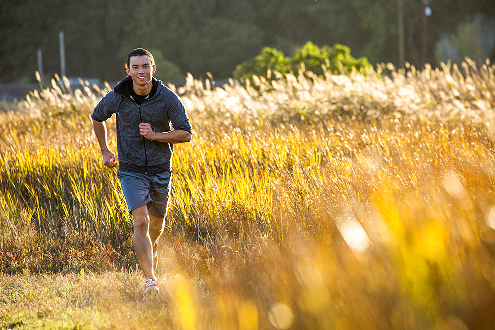 Smiling Mixed Race man running in field