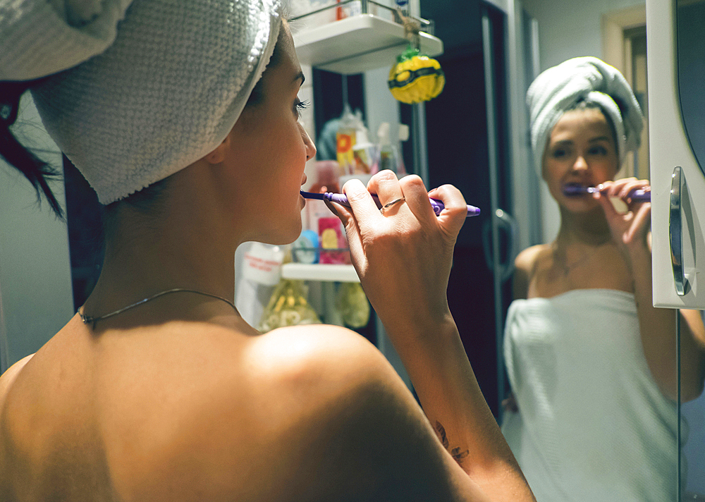 Caucasian woman brushing teeth in mirror