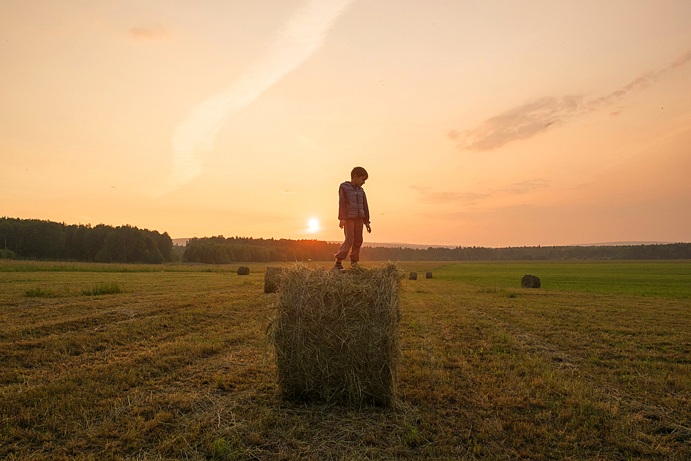 Mari boy standing on hay bale in field, Ural, Russia