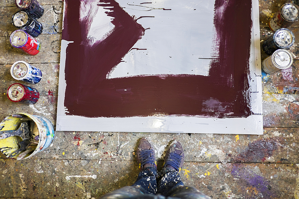 Legs of Mari man standing near paint cans and canvas on floor