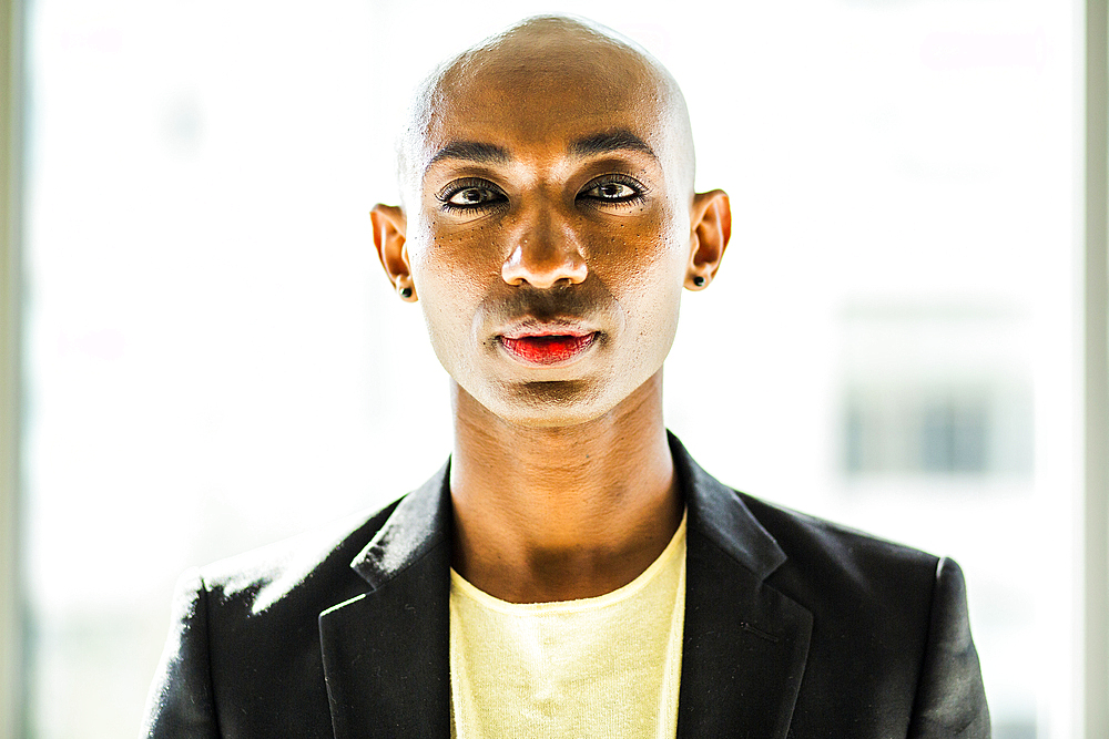 Serious gay Black man posing near window