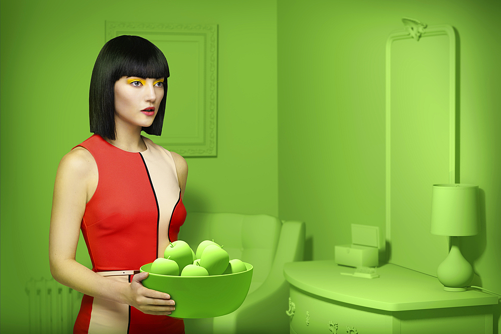 Caucasian woman in green old-fashioned bedroom carrying bowl of apples