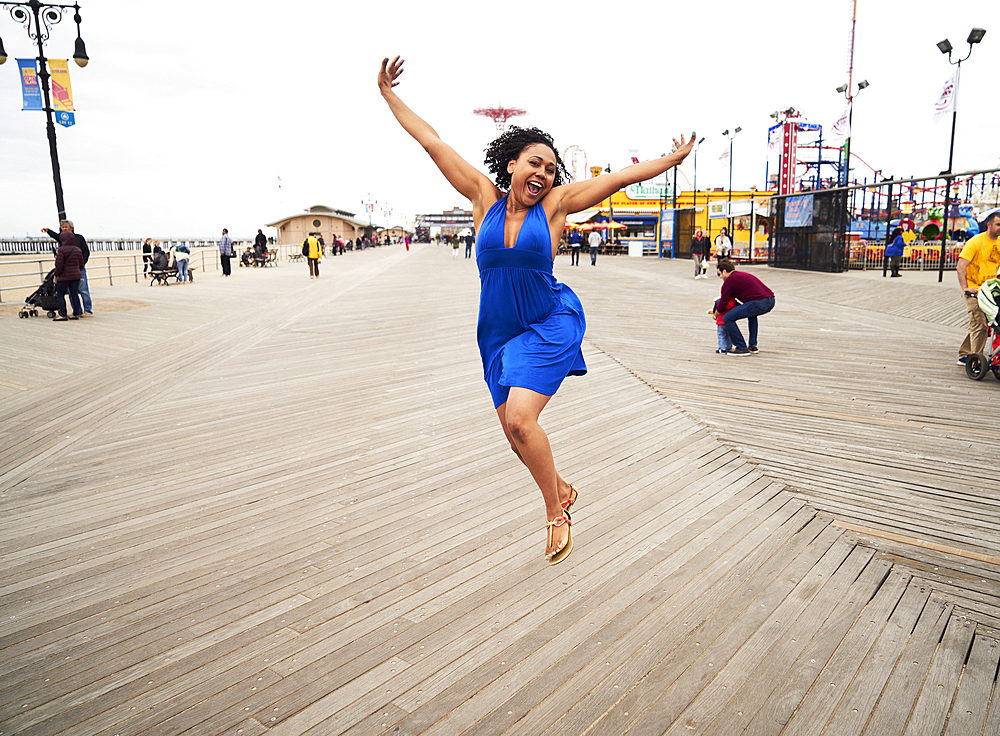 Woman smiling and jumping on boardwalk at amusement park