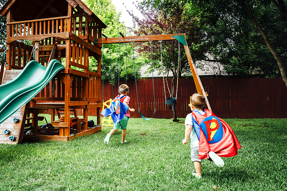 Caucasian brothers wearing superhero costumes in backyard