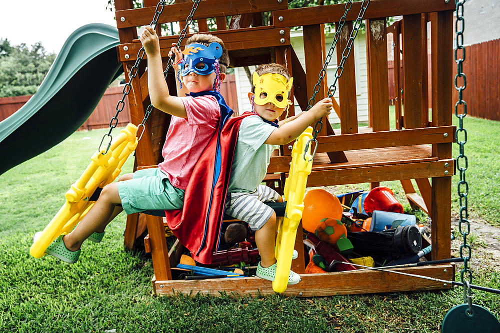 Caucasian brothers wearing superhero costumes on swing