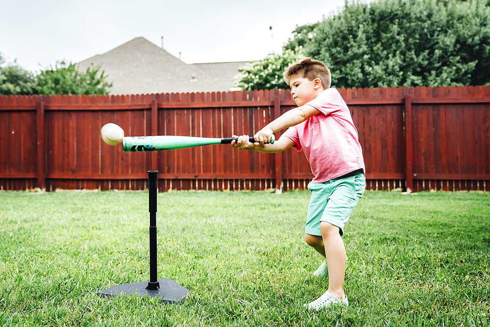 Caucasian boy hitting baseball off tee in backyard