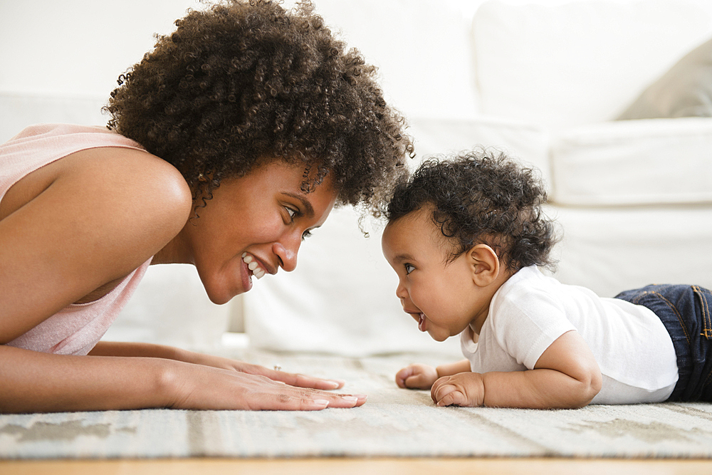 Mother playing face to face with baby son on floor