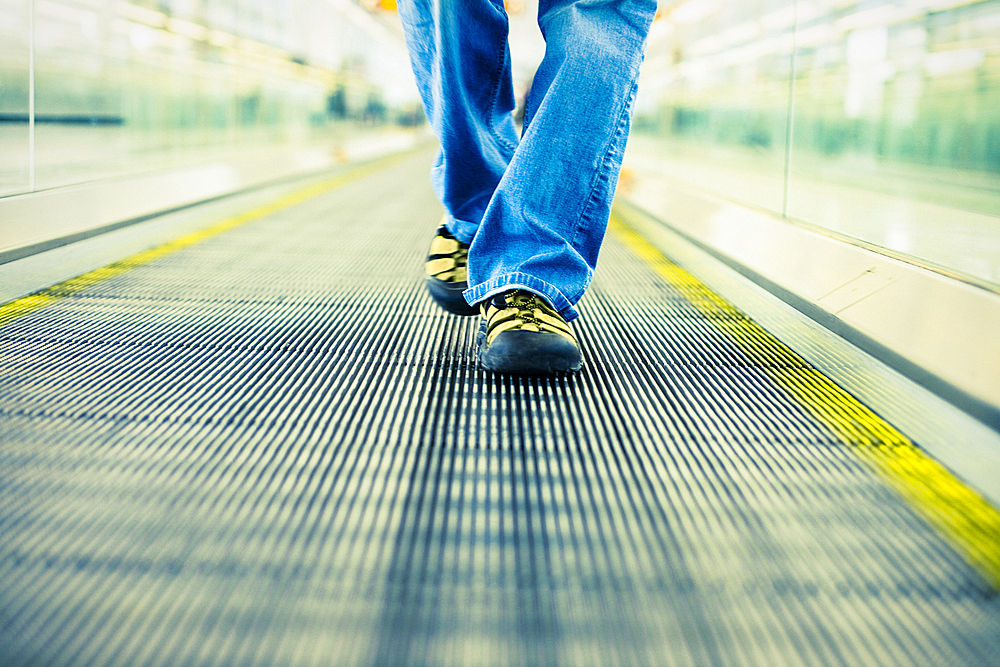 Legs of Japanese woman wearing jeans walking on moving walkway