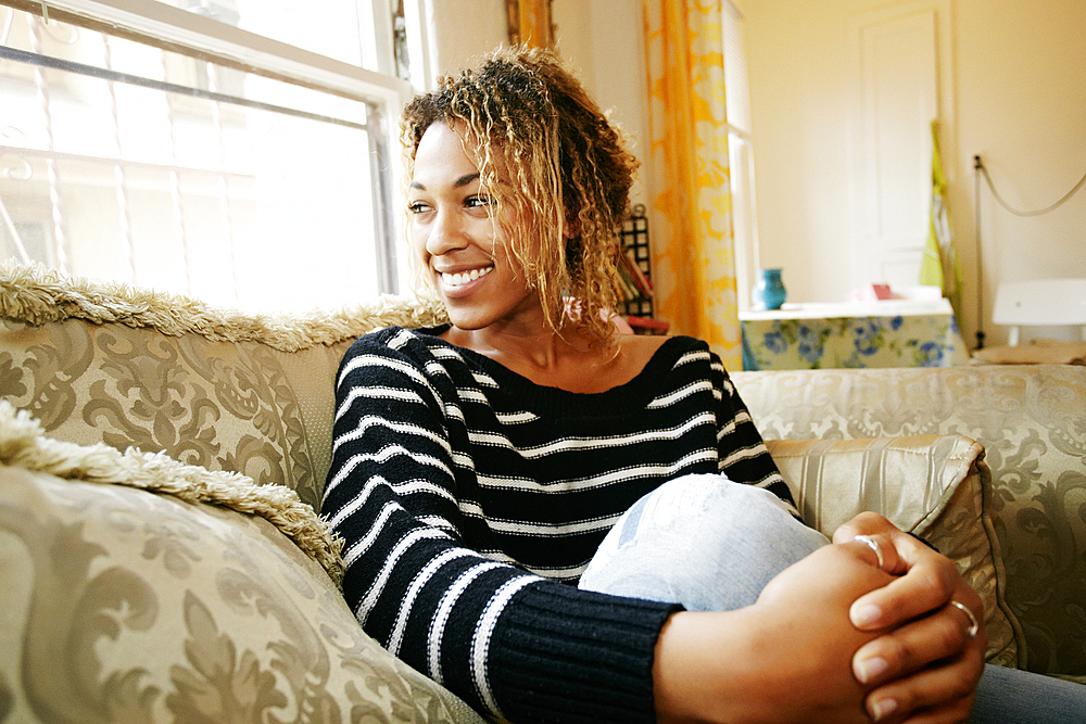 Smiling Mixed Race woman sitting on sofa at window