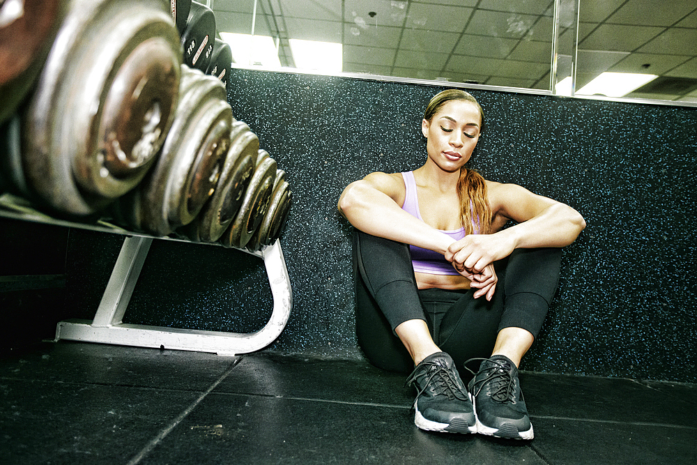 Mixed Race woman sitting on floor resting in gymnasium