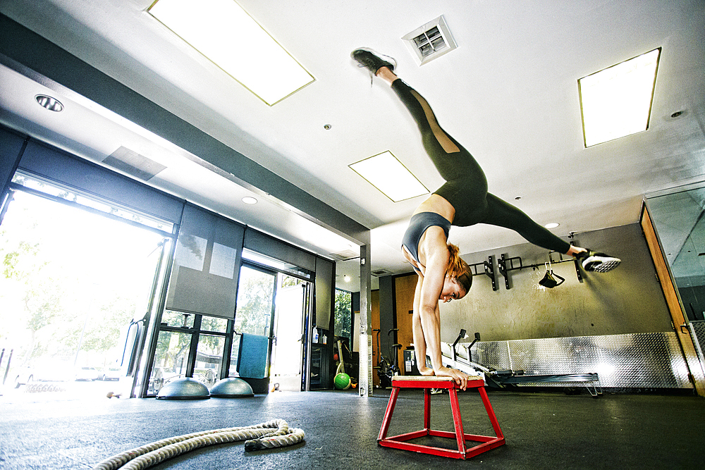 Mixed Race woman doing handstand on stool in gymnasium