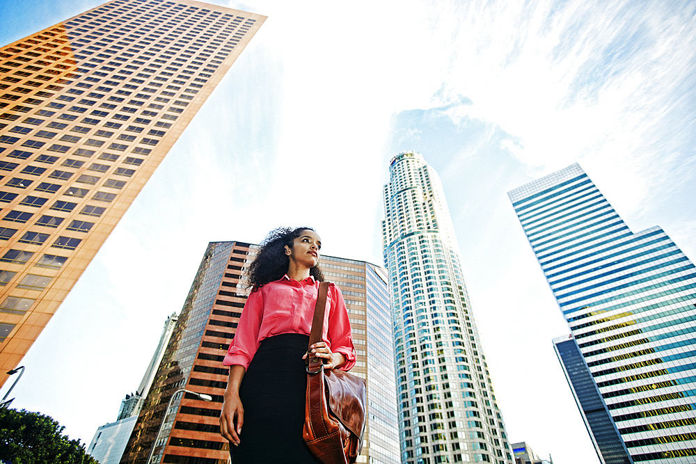 Serious Hispanic businesswoman near highrises in city