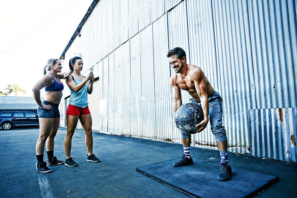 Women watching man lifting heavy ball outdoors