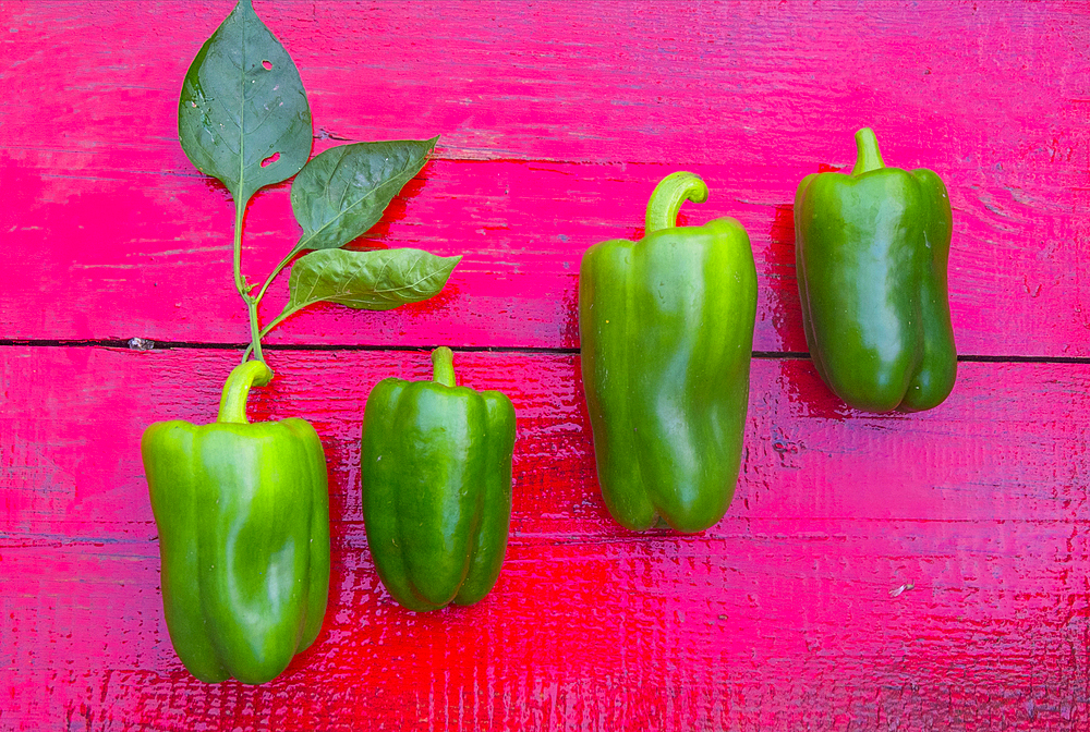 Close up of row of green peppers on red wooden table