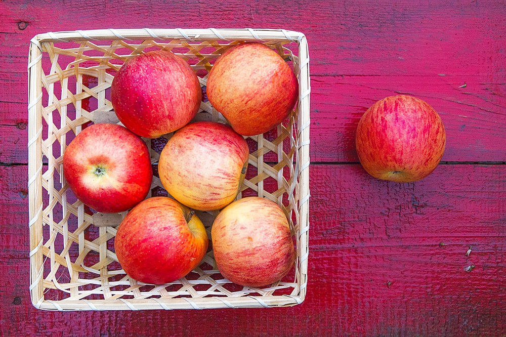 Close up of basket of red apples on red wooden table