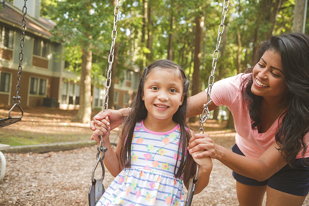 Hispanic mother pushing daughter in playground swing