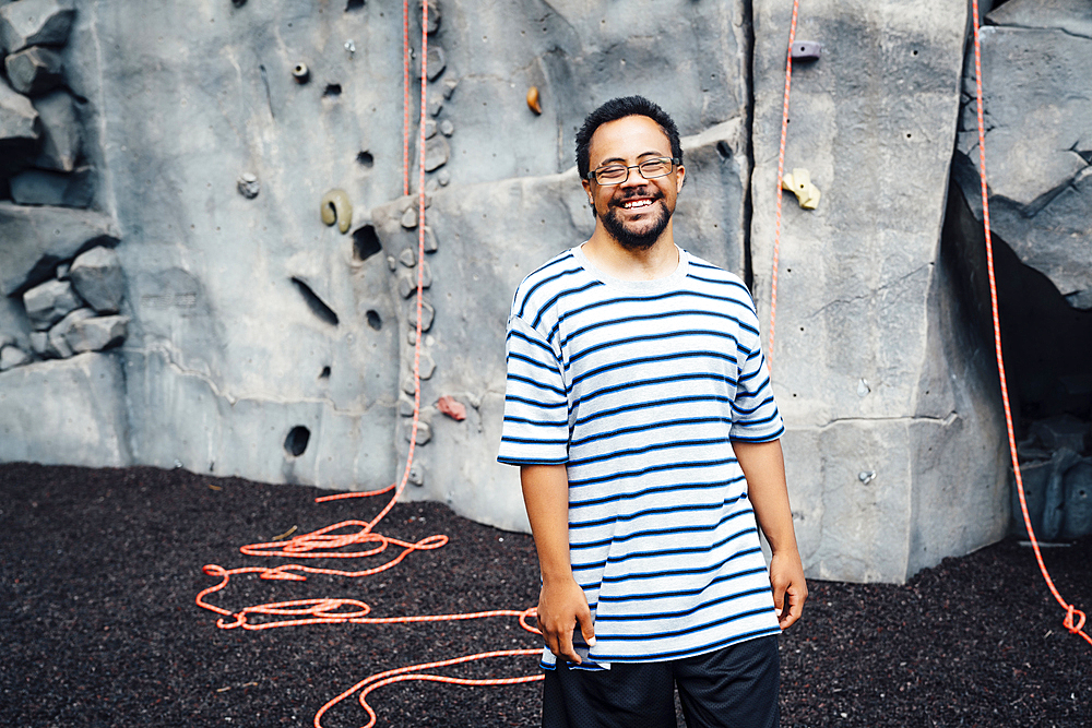 Mixed Race man smiling near rock climbing wall