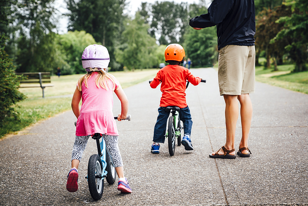 Father watching daughter and son riding bicycles