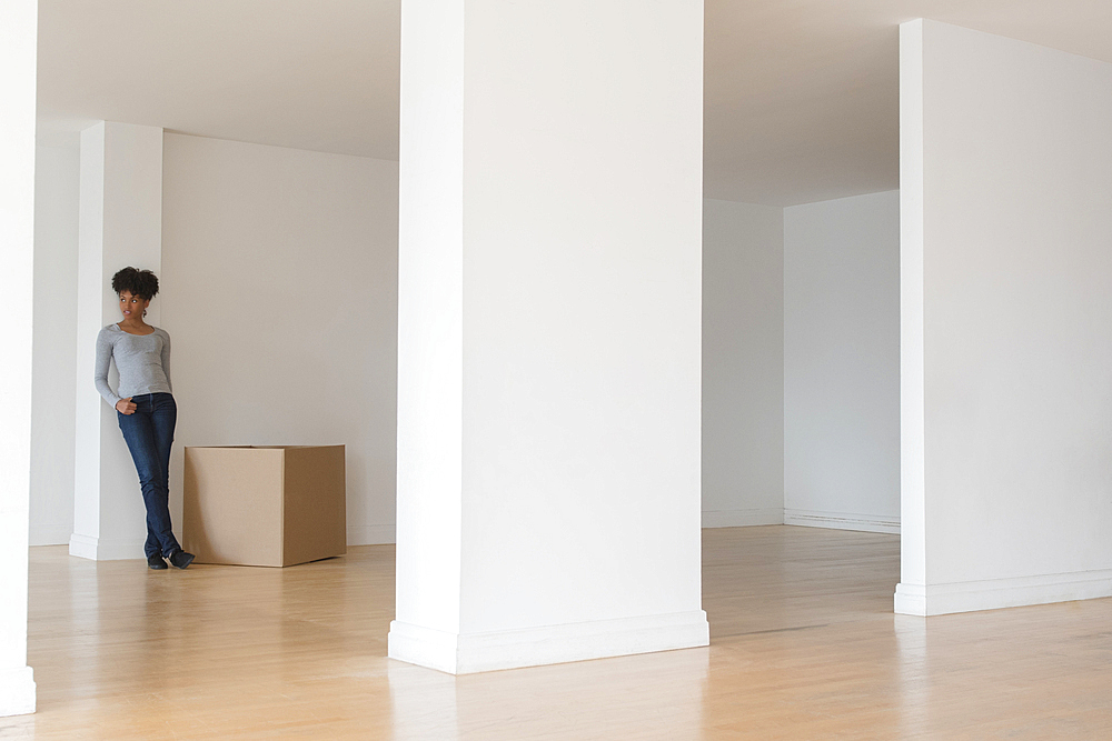 Black woman leaning on pillar in empty apartment